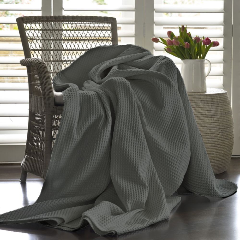 Grey textured blanket draped over a chair in a room with a window and plant.