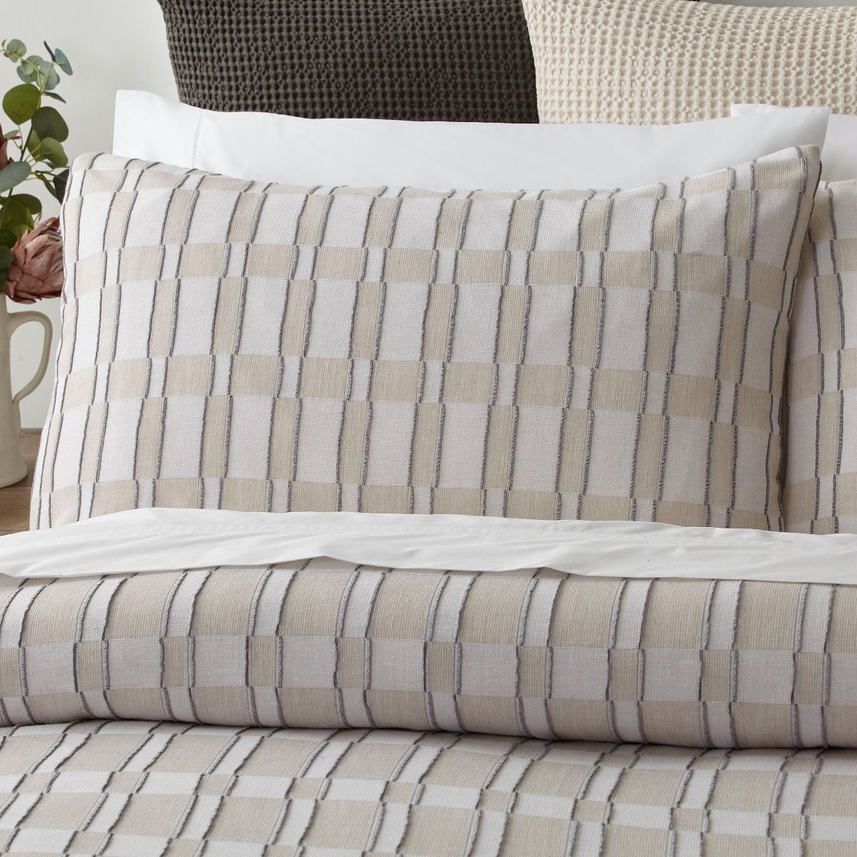 Closeup image of a Checkered bedspread in Beige and White colours and pillows on a bed.