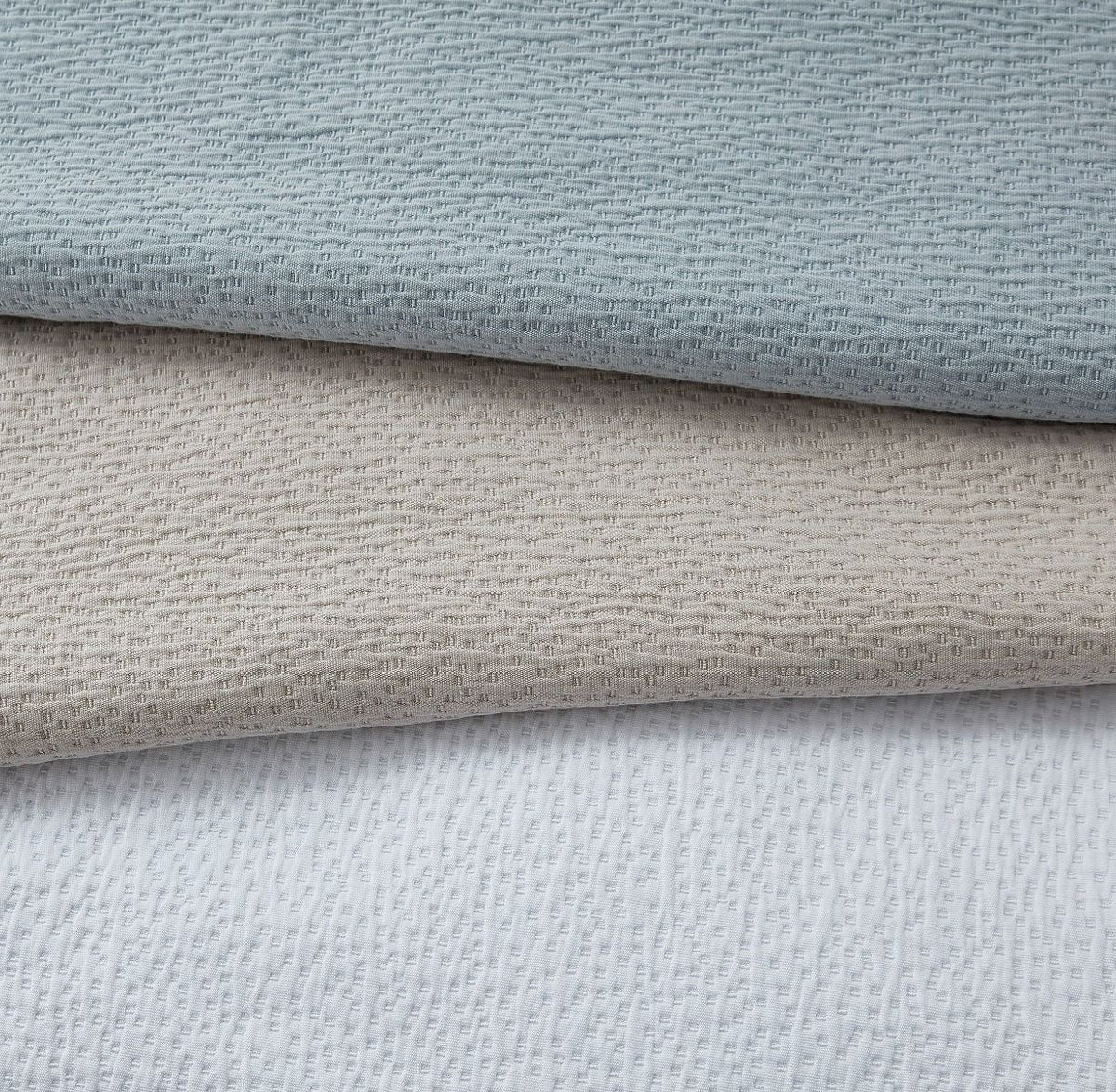 Three swatches of the textured bedspread in fabric. The colours are Duck Egg blue, Ecru but it looks more Beige, and White.