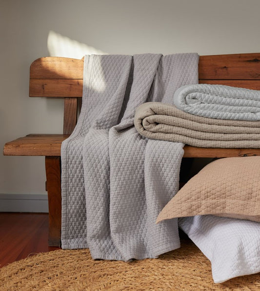 Stack of folded blankets in various colors on a wooden bench.