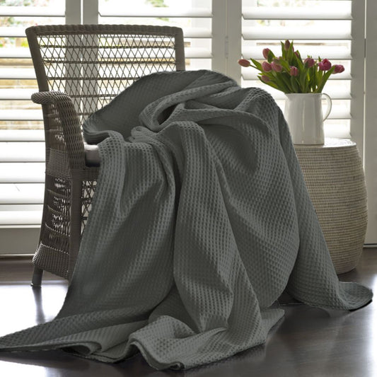 Grey textured blanket draped over a chair in a room with a window and plant.
