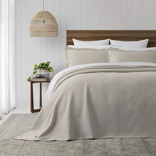 Neatly made bed with a beige textured bedspread in a bedroom setting.