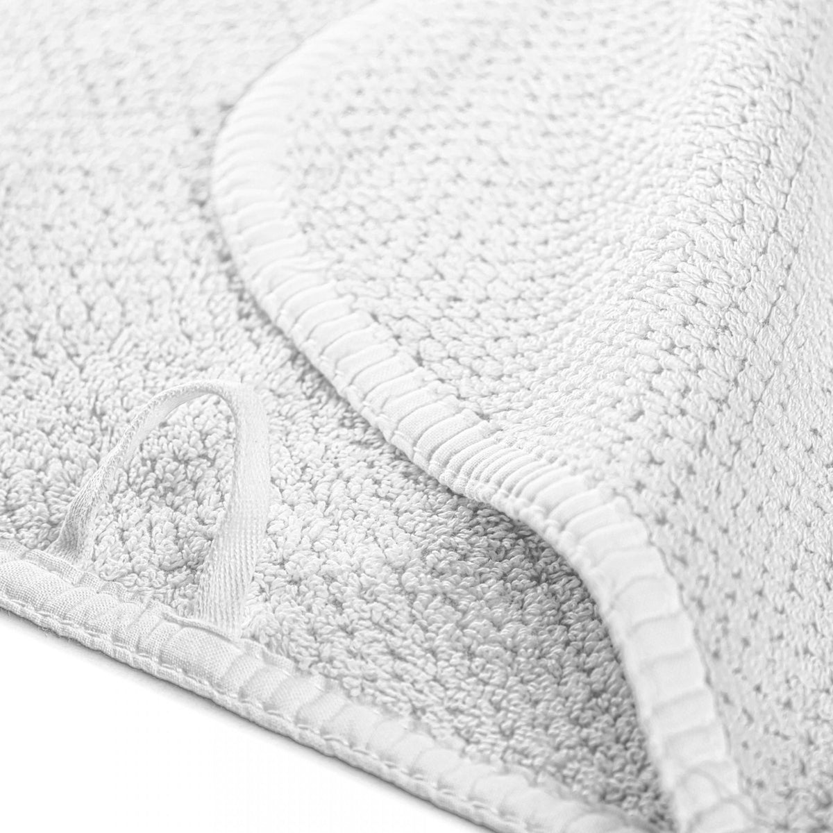 A close-up of a white textured fabric item, likely a towel or blanket, folded over to show its looped corner and ribbed stitched edge.