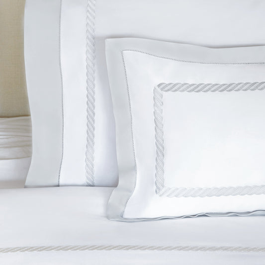 White bedding set with decorative rope-embroidered borders on the pillowcases and matching sheet, shown in a clean close-up studio-style shot.