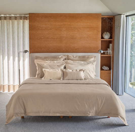 A neatly made bed with a Taupe bedding called the Vincent by BOVI and matching pillows, set against a light wood headboard and built-in shelving in a bright, modern bedroom.