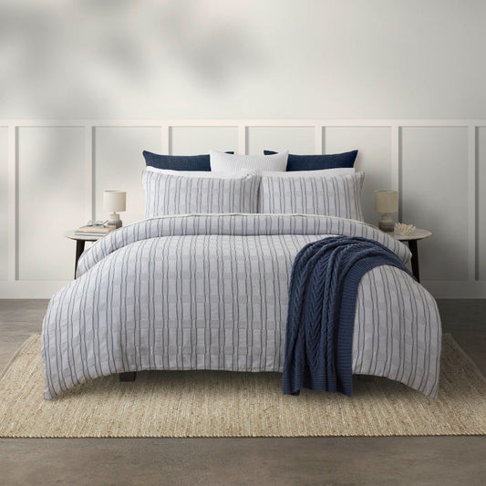 Bed with striped bedding and blue throw blanket in a bedroom setting.